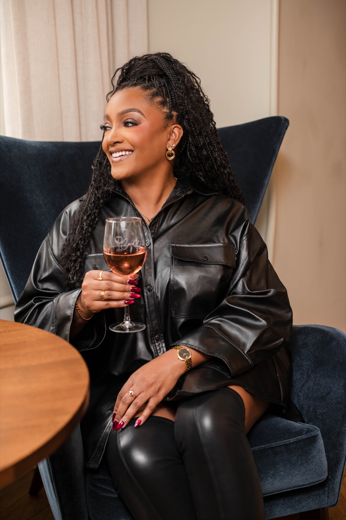 A woman seated in a velvet chair, smiling and holding a glass of rose wine